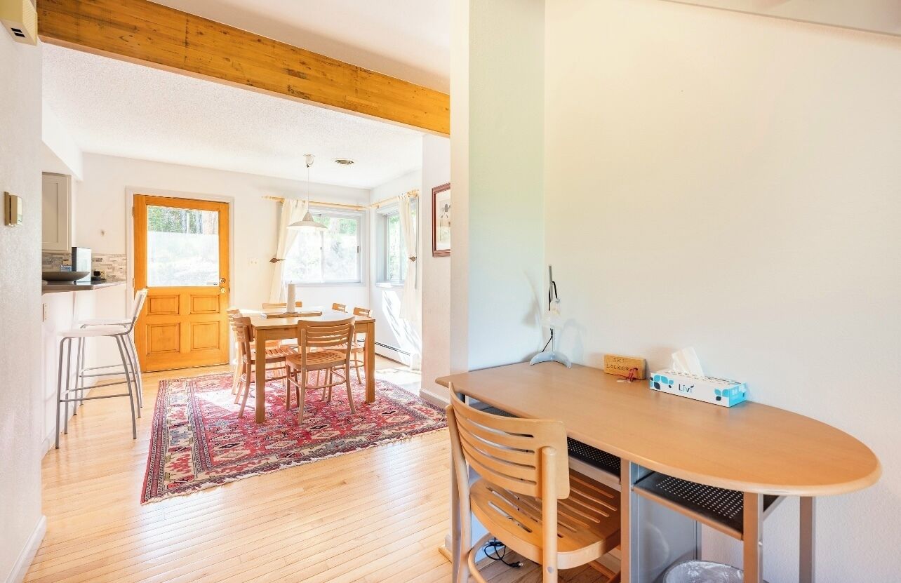Un coin repas avec une table et des chaises en bois, un tapis, et une cuisine visible au fond.