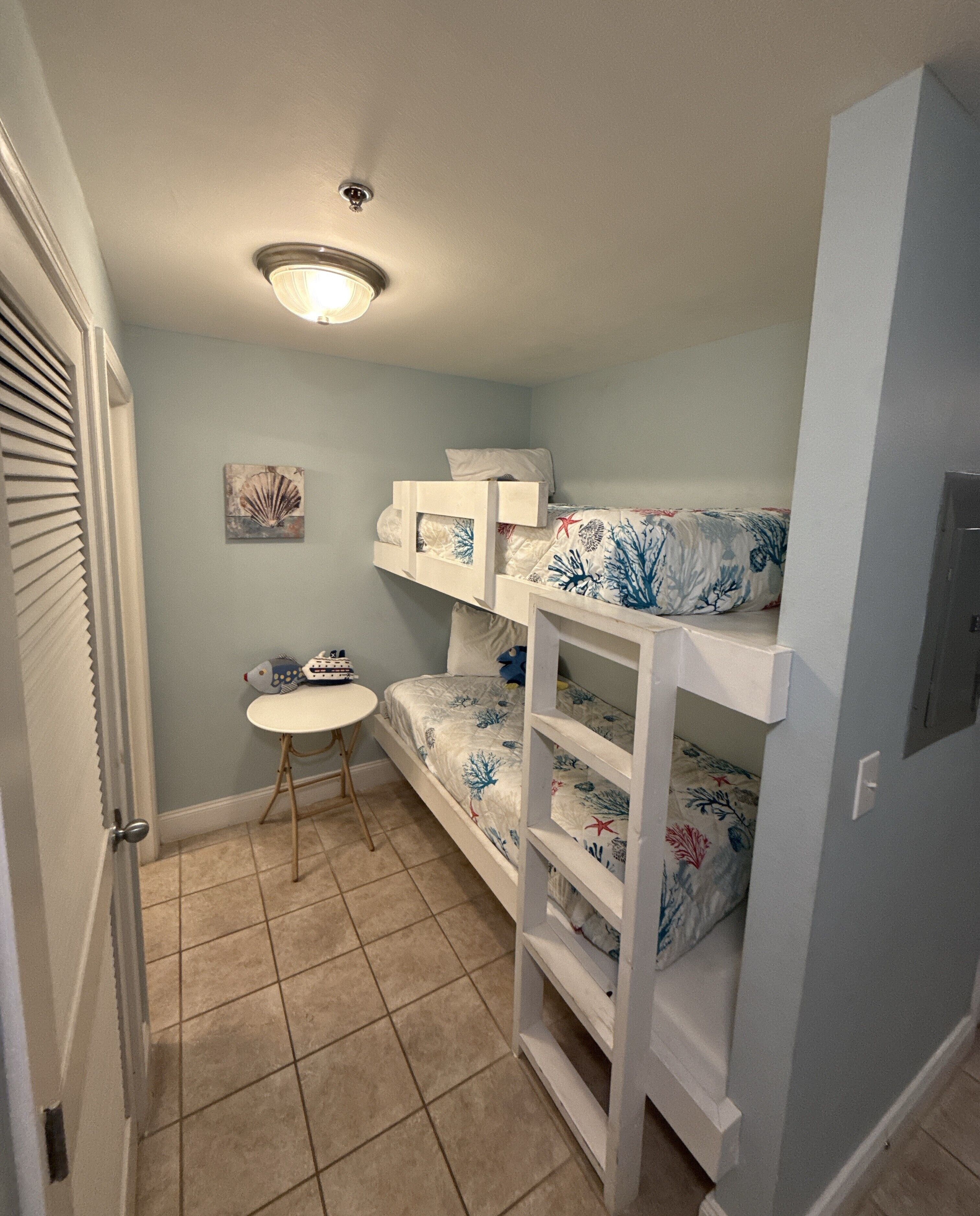 Une chambre à coucher de taille réduite, avec des lits superposés, une petite table ronde et un luminaire fixé au plafond.