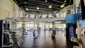 Una palestra su più livelli con diverse attrezzature, ampie finestre e un soppalco.