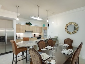 A modern kitchen with stainless steel appliances, a dining area with a round table and patterned chairs, and pendant lighting.