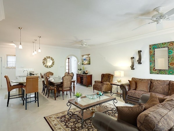 A spacious living room with a dining area, a ceiling fan, and a large mirror on the wall.