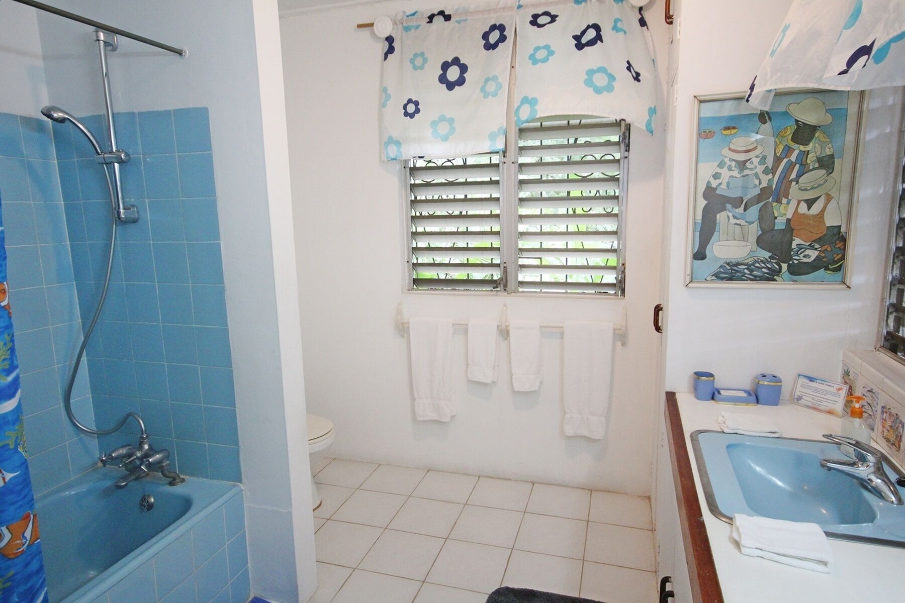 A bathroom with a shower, toilet, sink, and a window with shutters.