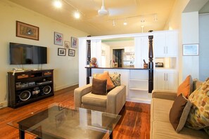 A living room with a glass coffee table, two sofas, a television, and a kitchen area in the background. - Beachfront Classic 3-bed House - Whitecaps by BSL Rentals (Mullins)
