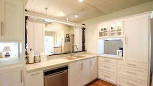 Una cocina con armarios blancos, lavavajillas, un lavabo y un refrigerador.