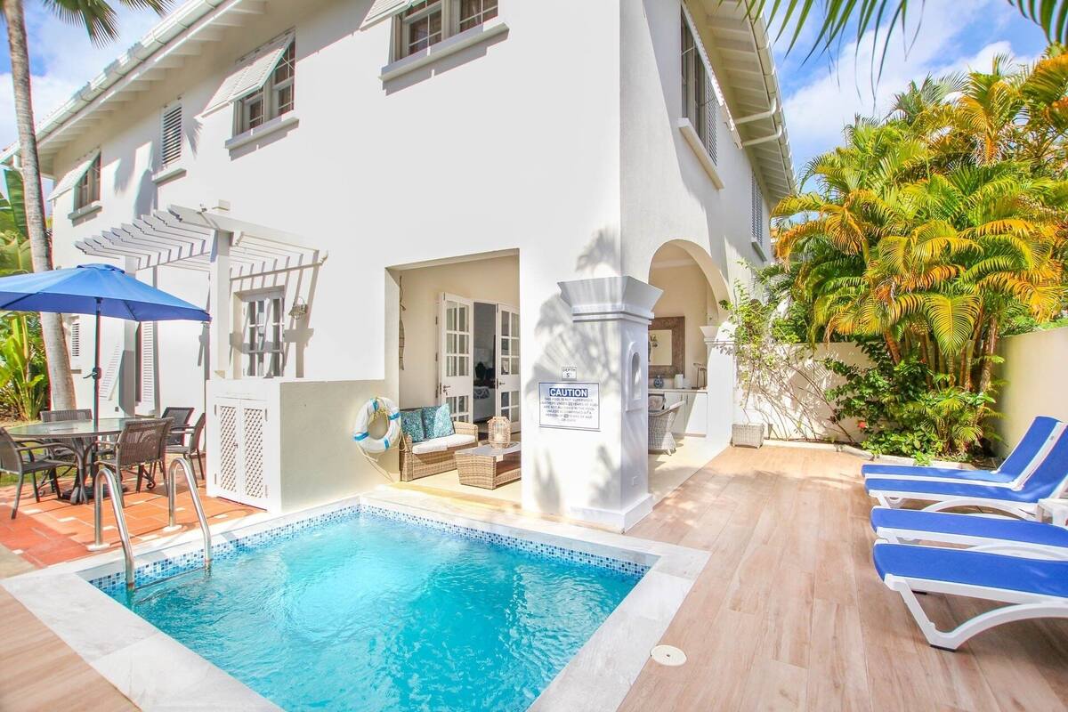 A pool area with a white building, lounge chairs, and a dining set.