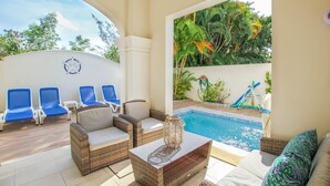 Un espace aménagé au bord de la piscine, avec des chaises longues, un canapé en osier et une petite table.