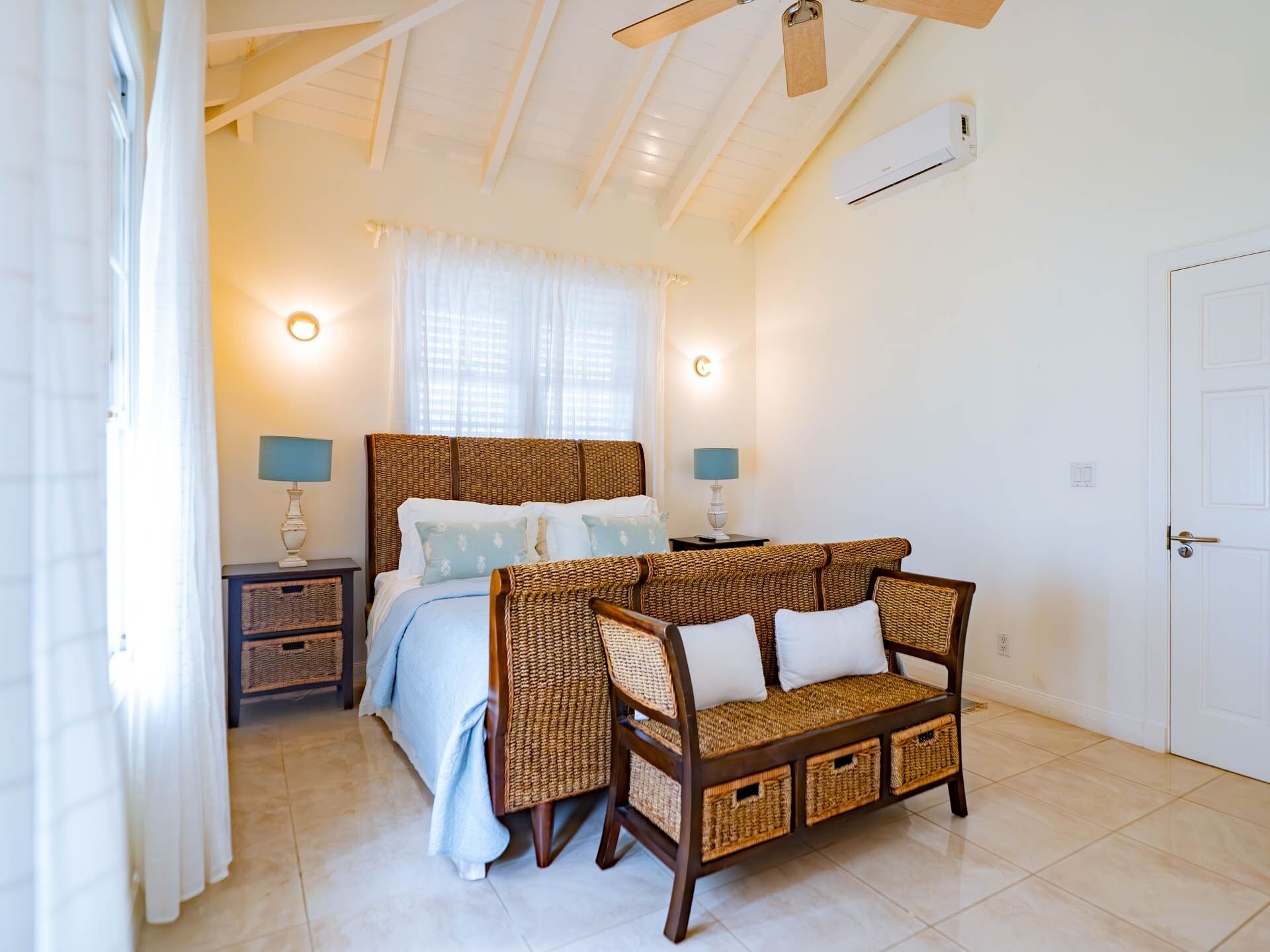 A bedroom with a bed, two bedside tables with lamps, a wicker sofa, and a ceiling fan.