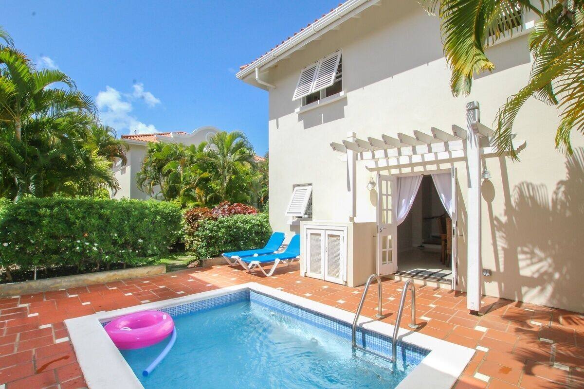 A swimming pool with a pink float ring, blue lounge chairs, and a white pergola.