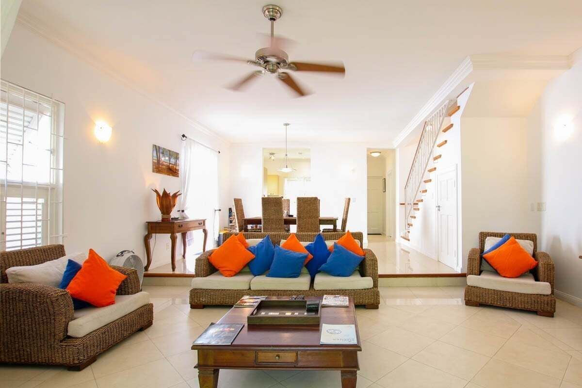 A spacious living room with a ceiling fan, wicker furniture, and a dining area in the background.