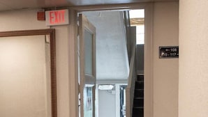 Un couloir avec un plancher en bois, un panneau indiquant la sortie et un escalier menant à un autre étage.