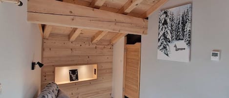 Una habitación acogedora con techo de madera, un sofá estampado con motivos de animales, una estantería montada en la pared y un cuadro enmarcado de un paisaje nevado.