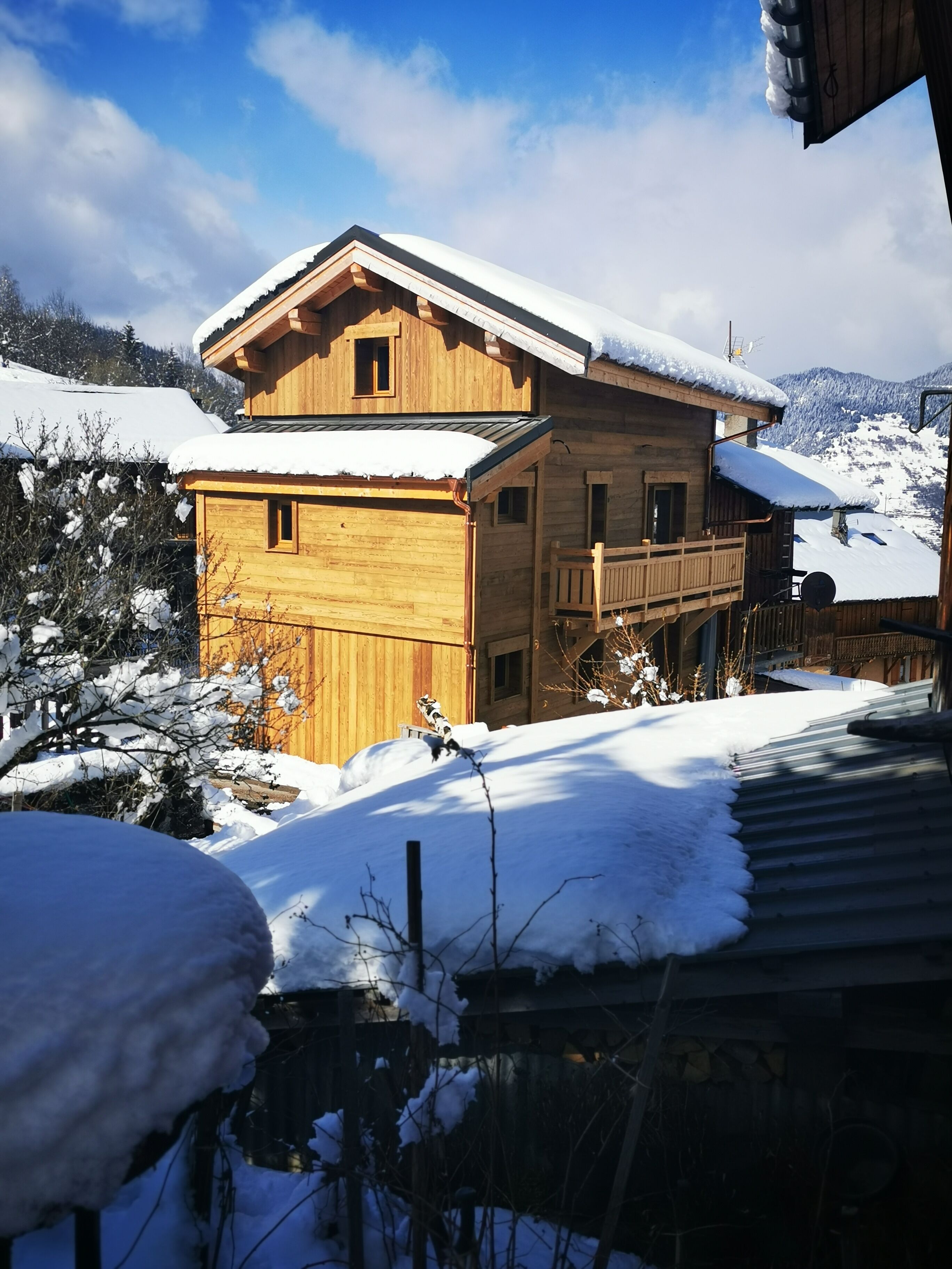 Un chalet en bois doté d’un balcon et d’un toit enneigé, niché au cœur d’un paysage montagneux.