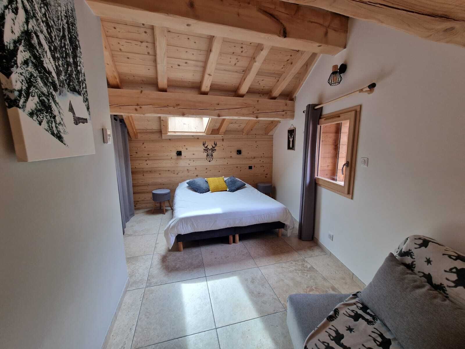 Een gezellige slaapkamer met een bed, een klein krukje, een raam en een houten plafond.