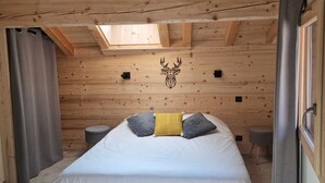 A wooden cabin bedroom with a bed, a skylight, and a deer head wall decal. - New chalet Méribel (Méribel)