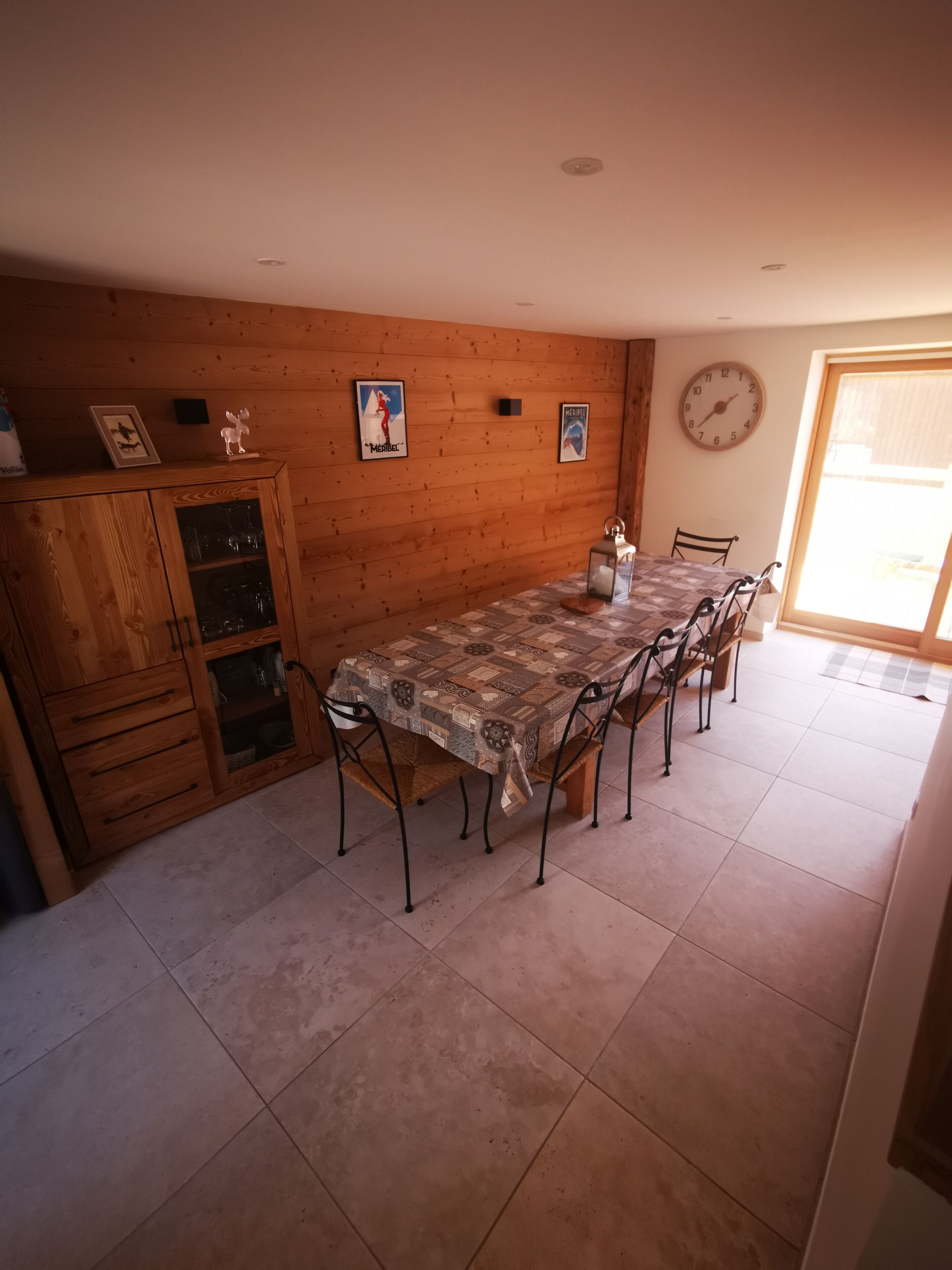 Een eetruimte met een lange tafel, stoelen, een houten kast en wanddecoraties.