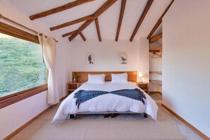 A bedroom with a large bed, wooden beams on the ceiling, a window with curtains, and a nightstand with a lamp. - Casa iLayaku (Guangopolo)