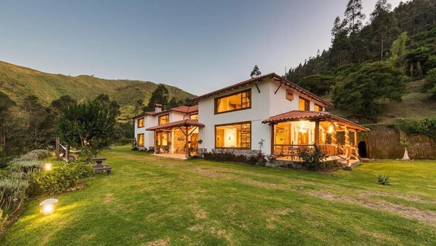 Une maison à deux étages dotée d’un patio, entourée d’une pelouse bien entretenue et d’arbres.