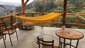 Une terrasse en bois avec un hamac, deux chaises et une table ronde.
