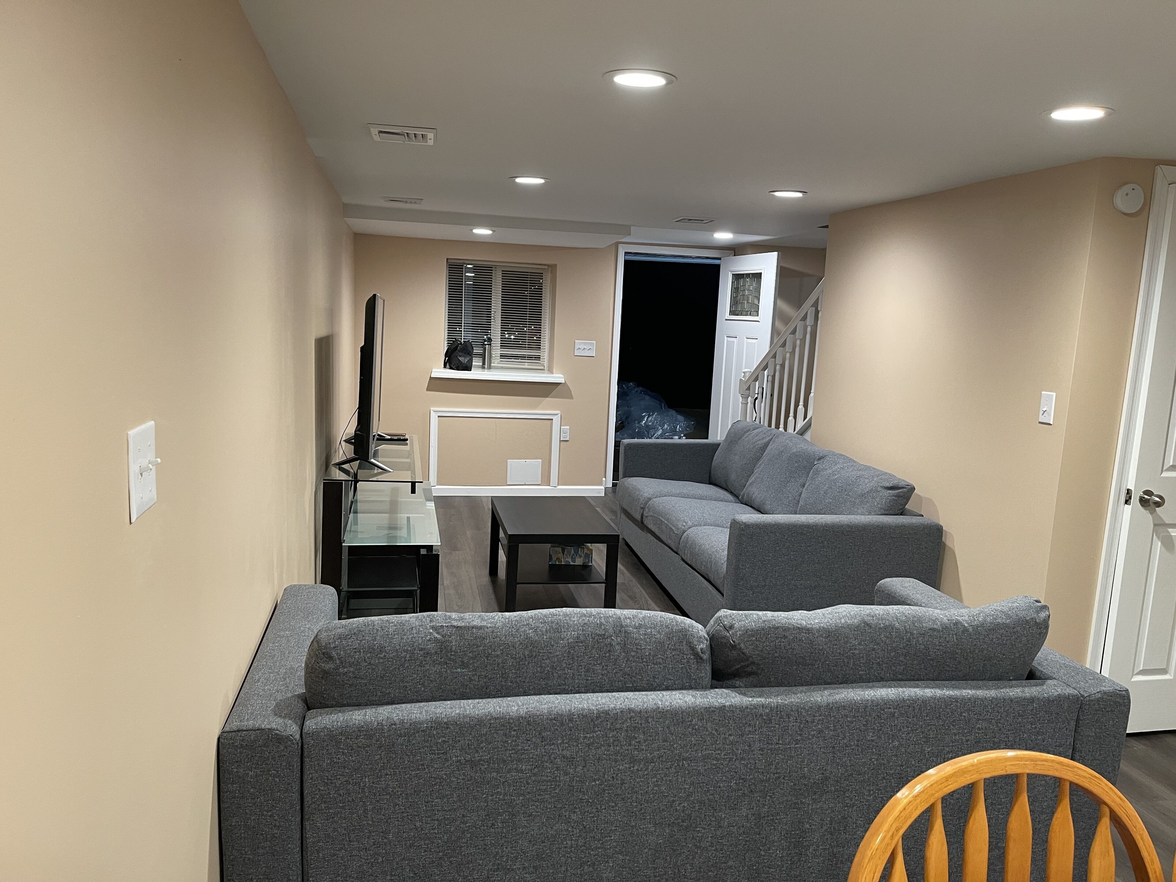 Una sala de estar con un sofá gris, una mesita y un televisor. Se ve una escalera que conduce a otra habitación.