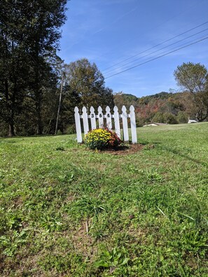 Surrounded by a white picket fence, this serene garden features a vibrant flower arrangement and a tranquil natural setting.
