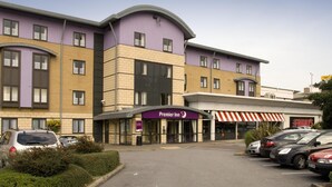 Un hôtel à la façade violette et beige, doté d’un parking et d’une devanture avec un auvent rouge et blanc.