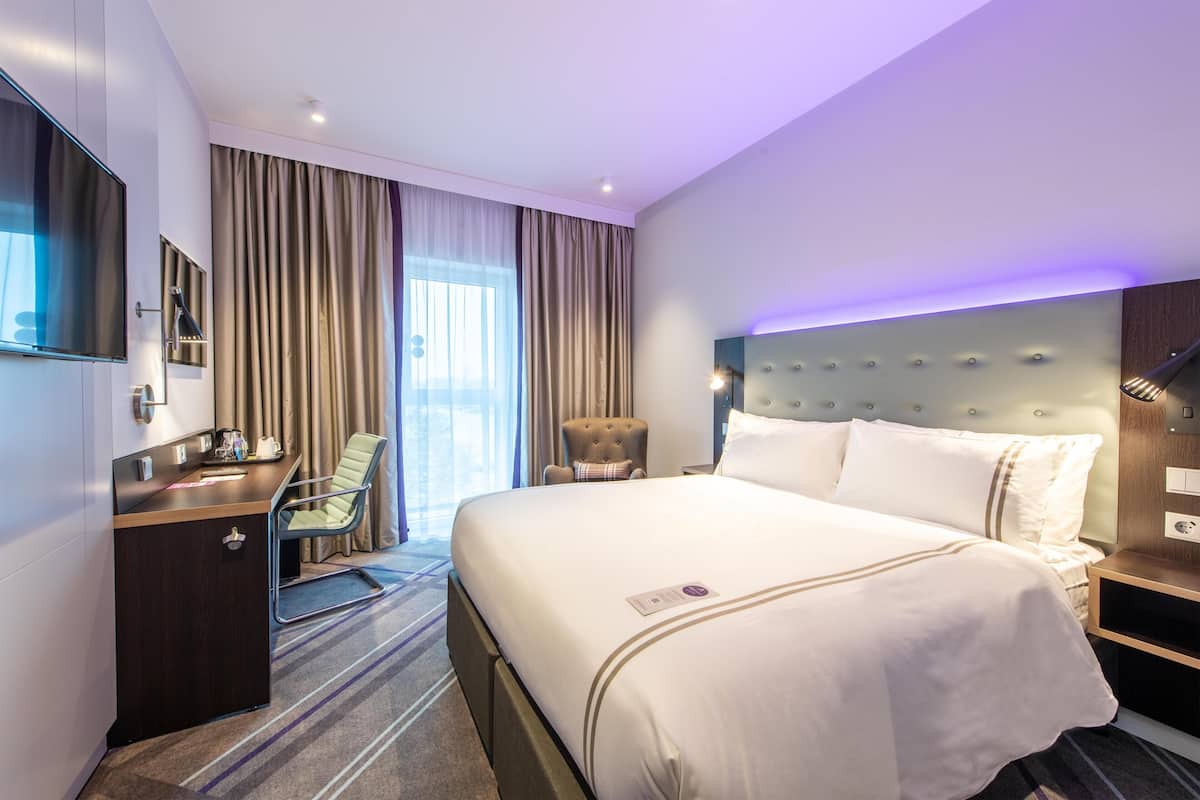 A hotel room with a bed, a desk, a chair, a TV, and a large window with curtains.