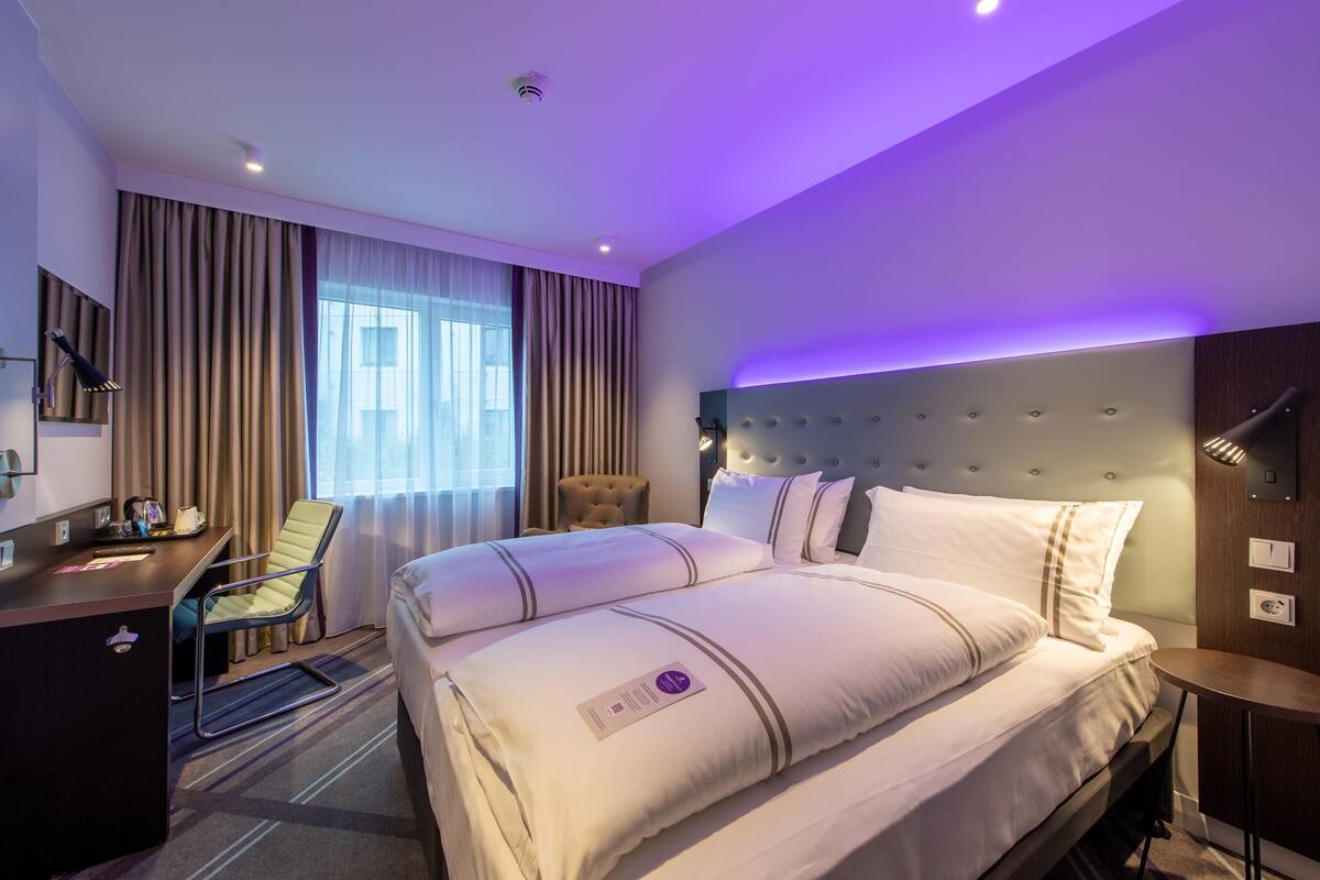 A hotel room with a large bed, a desk, a chair, and a small table.
