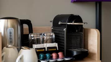 A coffee station with a coffee maker, a kettle, and a tray with coffee pods and a glass jar.