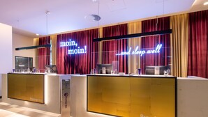 Uma área de recepção de hotel com dois balcões, um letreiro de neon e uma máquina de check-in.