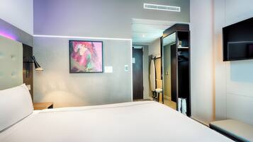 A modern hotel room with a large bed, a painting on the wall, a TV mounted on the wall, and a walk-in closet.