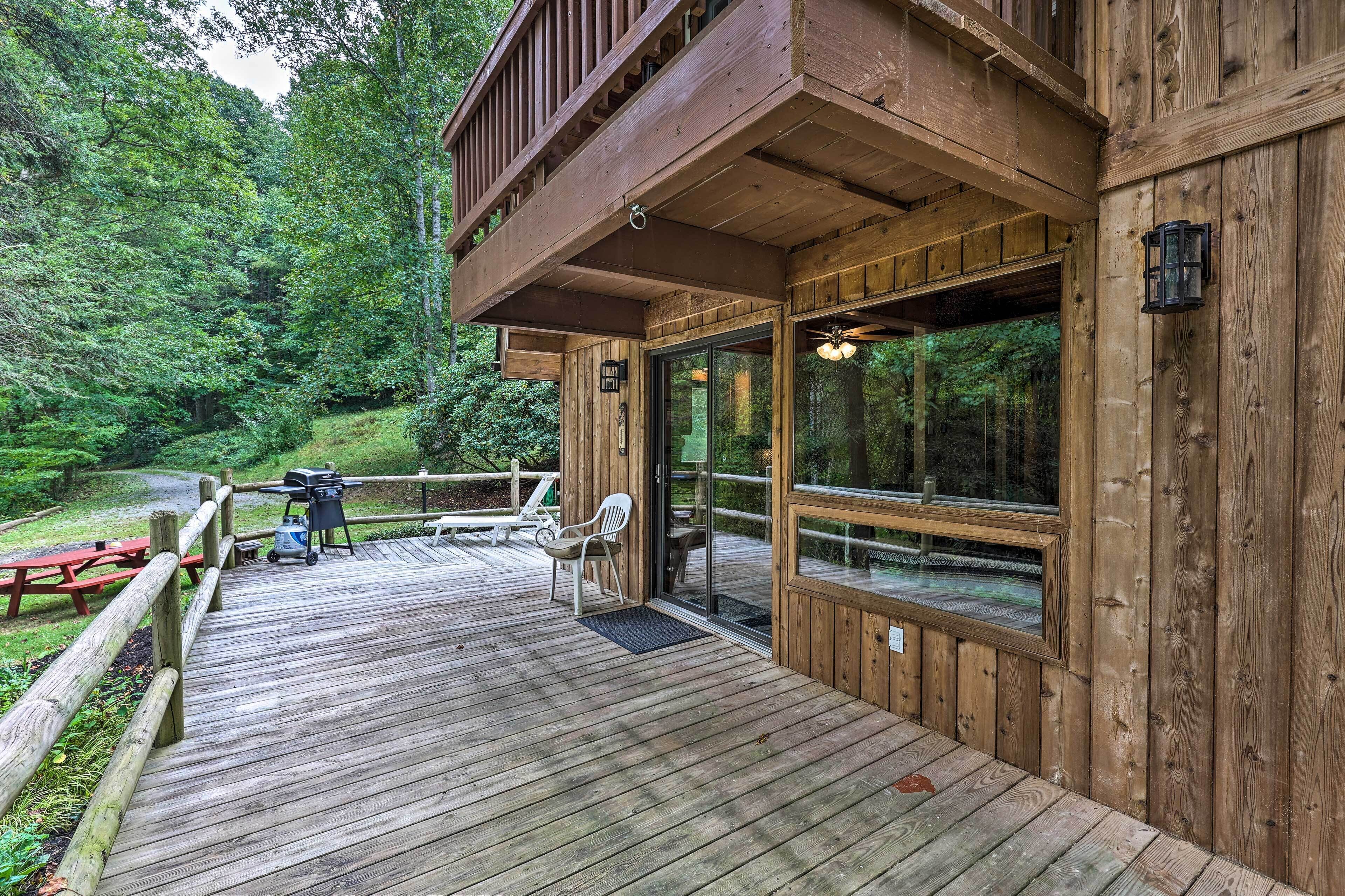 Une terrasse en bois avec une porte vitrée donnant sur un espace extérieur couvert, un barbecue et une chaise.