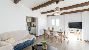 A modern living room with a sofa, dining table, and chairs. There is a kitchen area visible through an open doorway. - Casa Verde de Elena Benalauría by Ruralidays (Málaga)