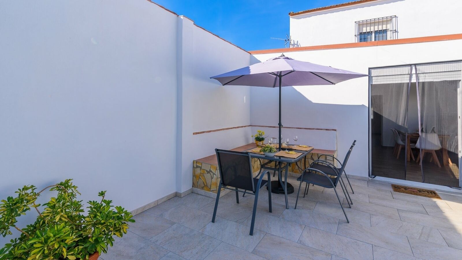 Un patio con una mesa y sillas, un paraguas morado y una planta en maceta.