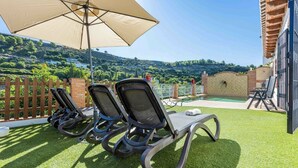 Een terras met drie loungestoelen, een grote parasol en uitzicht op een glooiend landschap.