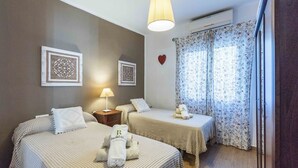 Een hotelkamer met twee bedden, een nachtkastje, een lamp, een hartvormige decoratie en bloemen gordijnen.