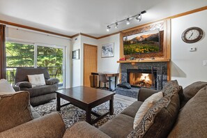 A living room with a fireplace, a sofa set, a dining area, and a large window.