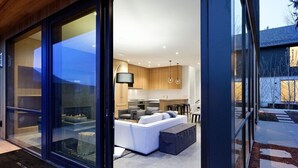 A modern interior with a large glass door leading to a living area featuring a white sofa and a dining table. - $7 Million Aspen 4BR Residence - Brand New Construction (Aspen)