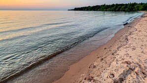 Ein Strand mit klarem Wasser und bewaldeter Küstenlinie im Hintergrund.
