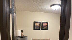 A compact kitchen with a refrigerator, a small table, and two framed pictures on the wall.