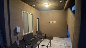 A covered patio area with a seating arrangement, a wall-mounted light fixture, and a window with frosted glass.