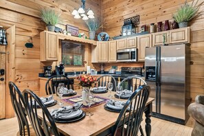 A wooden cabin-style kitchen with a dining table set for four, a refrigerator, and various kitchen appliances. - Pet Friendly! Views, Pool, 7mi to Dollywood, Golf (Sevierville)