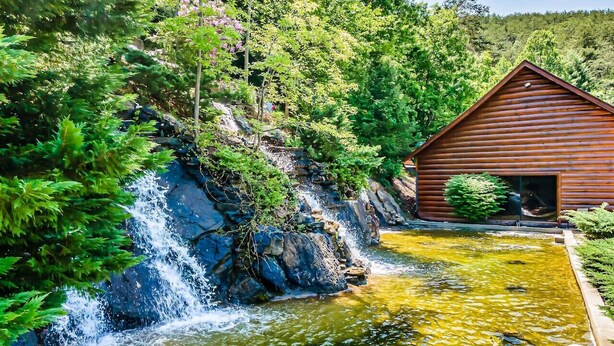 Een houten hutje met een waterval en vijver.