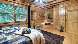 Een gezellig chalet met een bed, een plafondventilator, een raam met zonwering, een badkamer met badkuip en houten wanden.