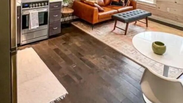 Una cocina compacta con estufa, microondas y armarios, una pared de piedra, un sofá de cuero marrón y una mesita con un bol verde.