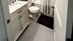 Un baño con lavamanos, inodoro y bañera blancos. Hay una cortina de ducha y una alfombra pequeña en el suelo.