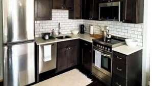 Una cocina moderna con armarios de madera oscura, electrodomésticos de acero inoxidable y un salpicadero de azulejos blancos.