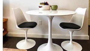 A small round table with two white chairs, a green mug, and a basket of items on the table. - Hip on Warren (Hudson)