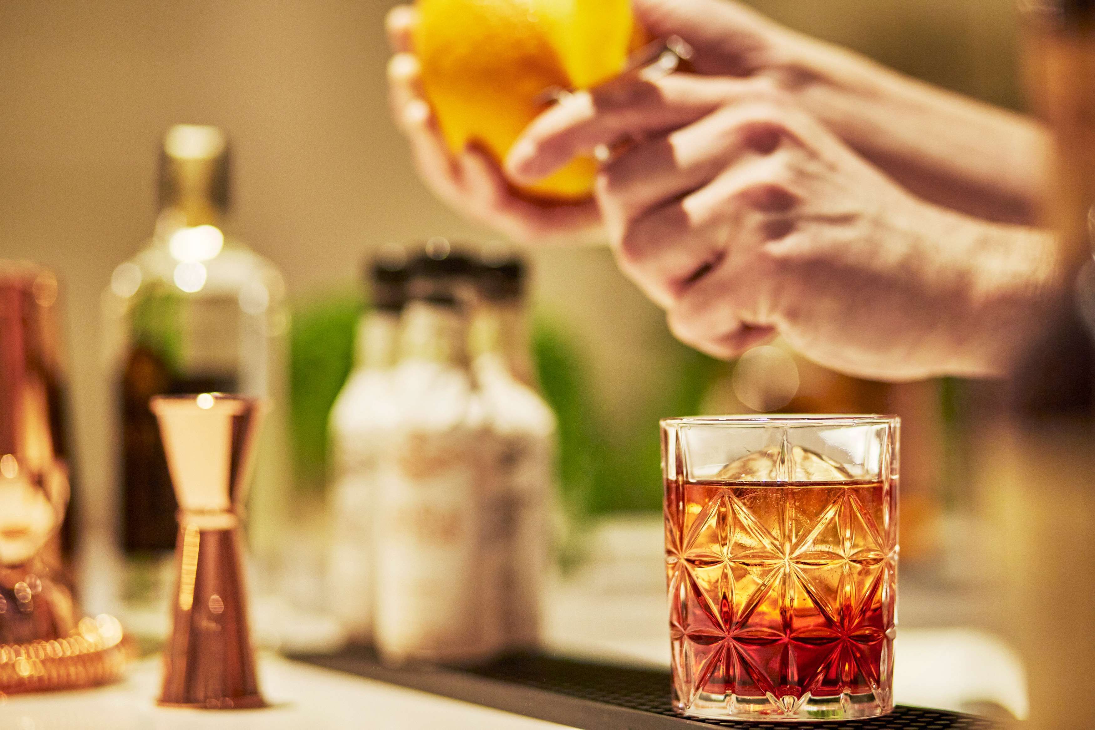A bar setting with a glass of amber-colored drink, a bottle, and a copper-colored object on the counter.