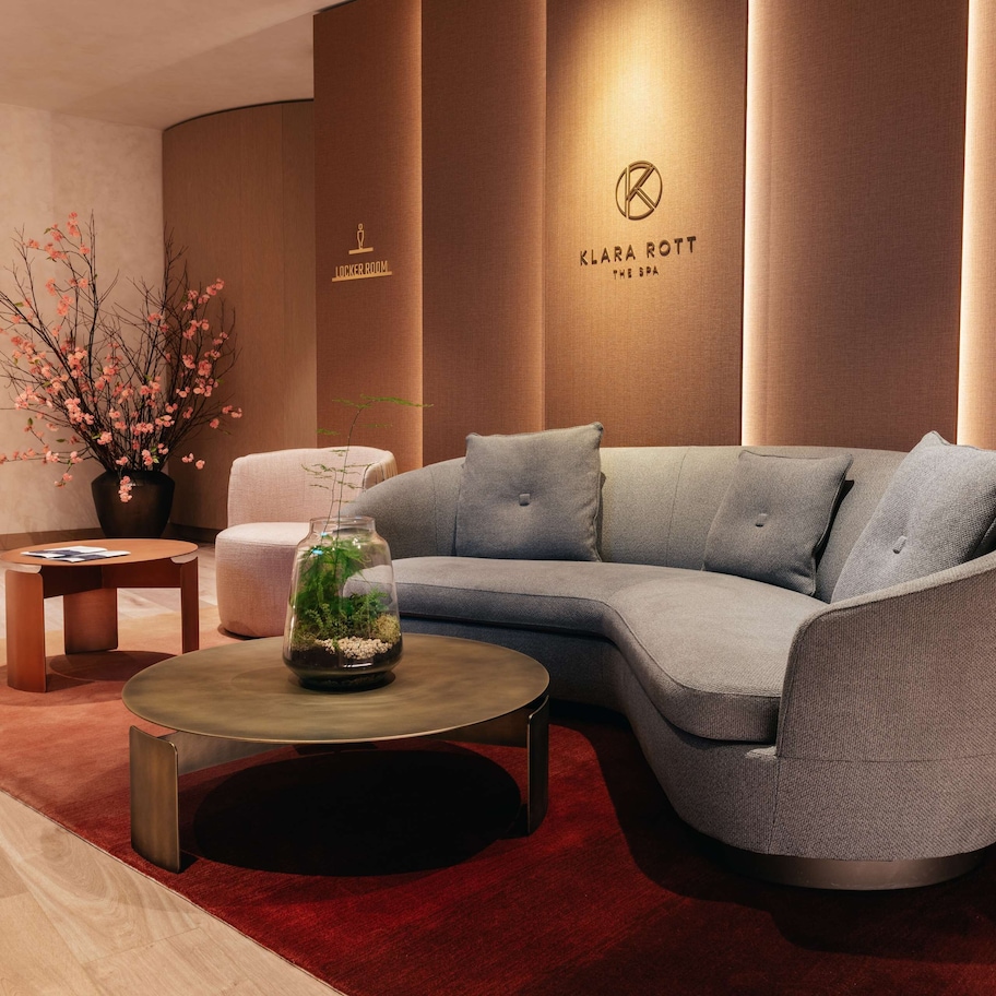 A modern living room with a grey sectional sofa, a round coffee table, and a vase with pink flowers.