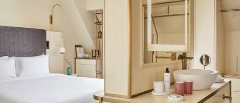 Una habitación de hotel moderna con una cama grande, un tocador con un espejo amplio y un lavabo redondo.